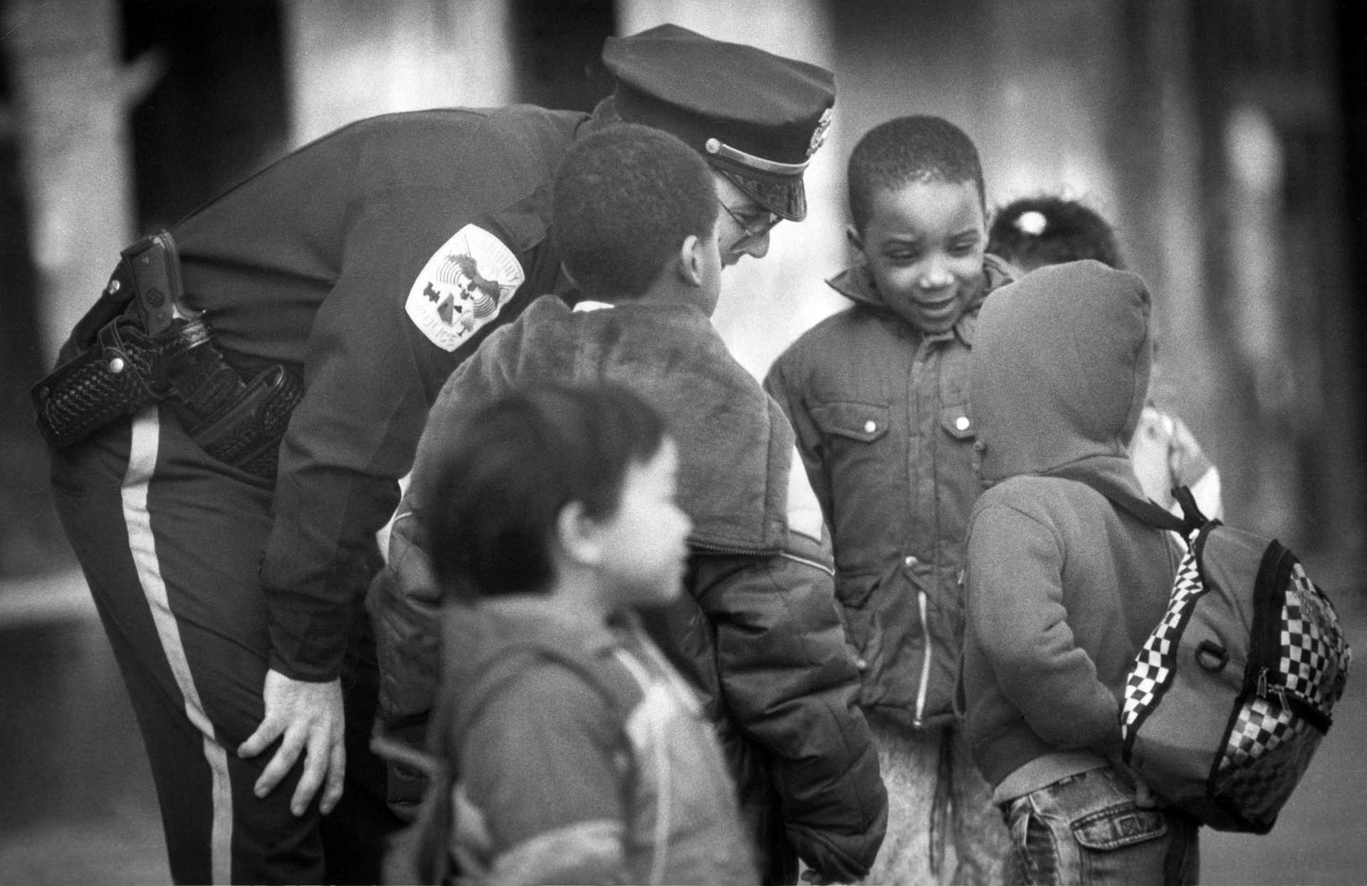 Danbury Police Officer Jim Marino stops to chat with school children waiting for the bus on Main Street. 1990.