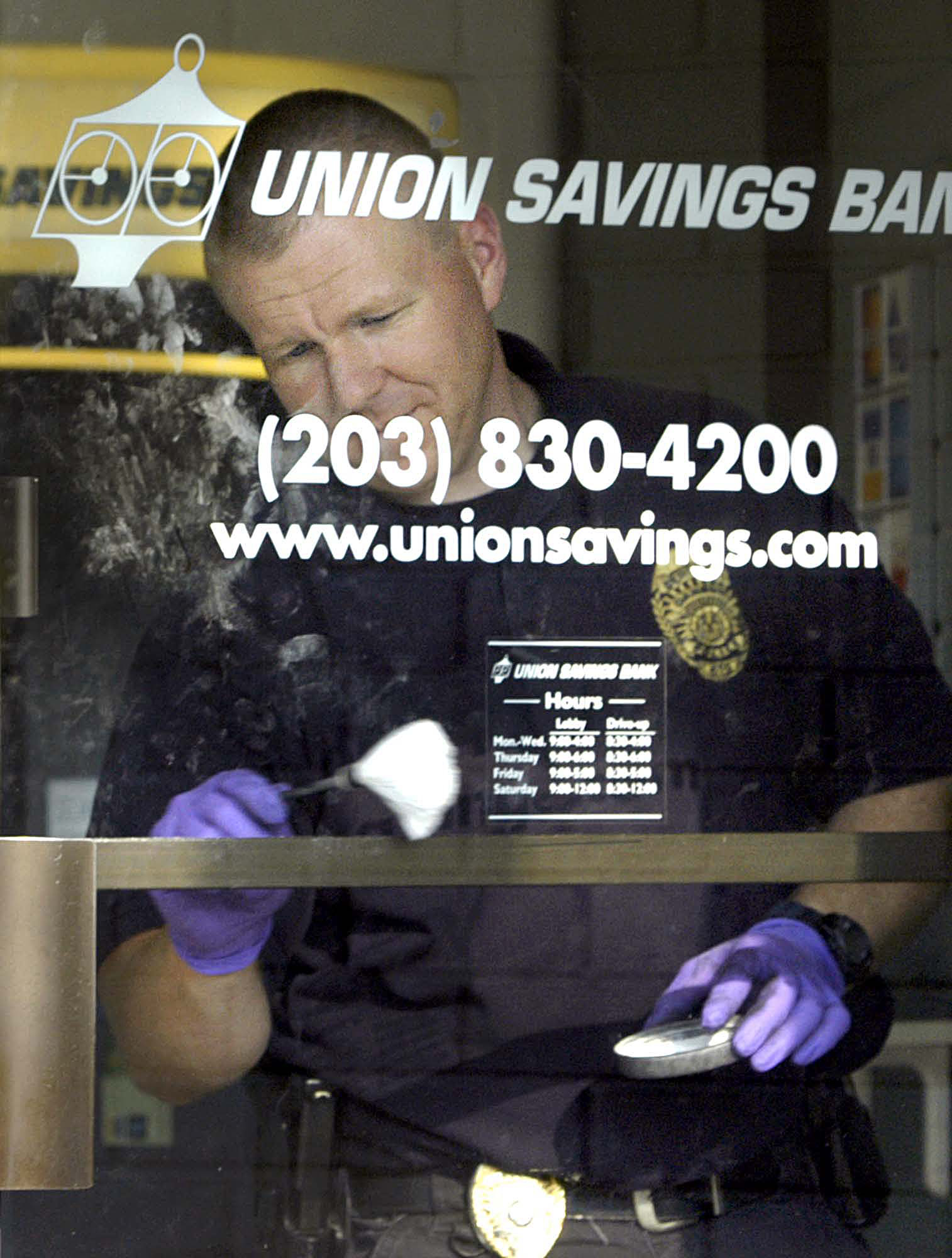 Danbury Police Sgt Bryan Bishop dusts for fingerprints on the front door of Union Savings Bank on Newtown Rd in Danbury after a bank robbery.