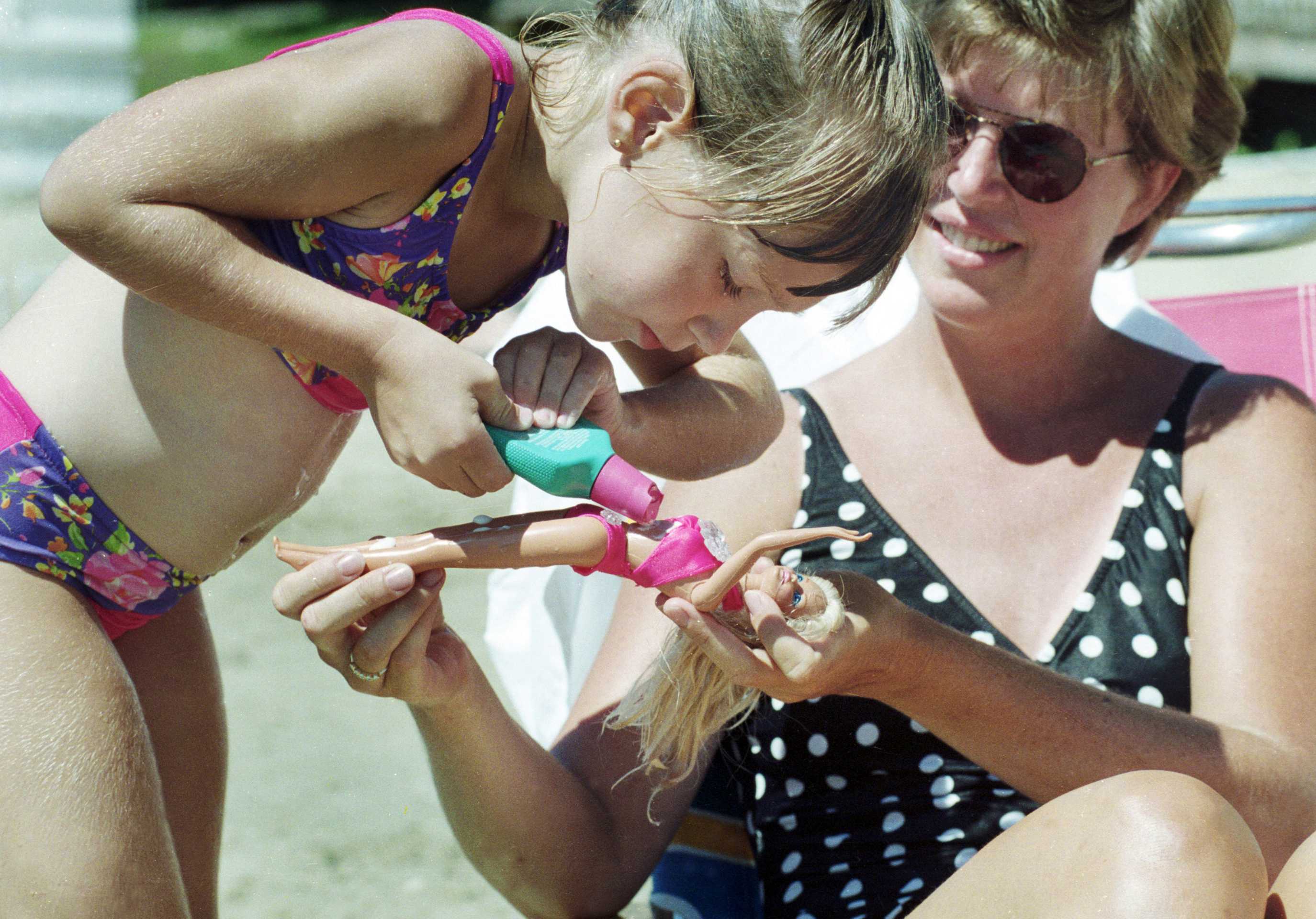 Little five-year-old Julia pours suntan lotion on her Barbie doll. Even Barbie has to be careful in the sun. 