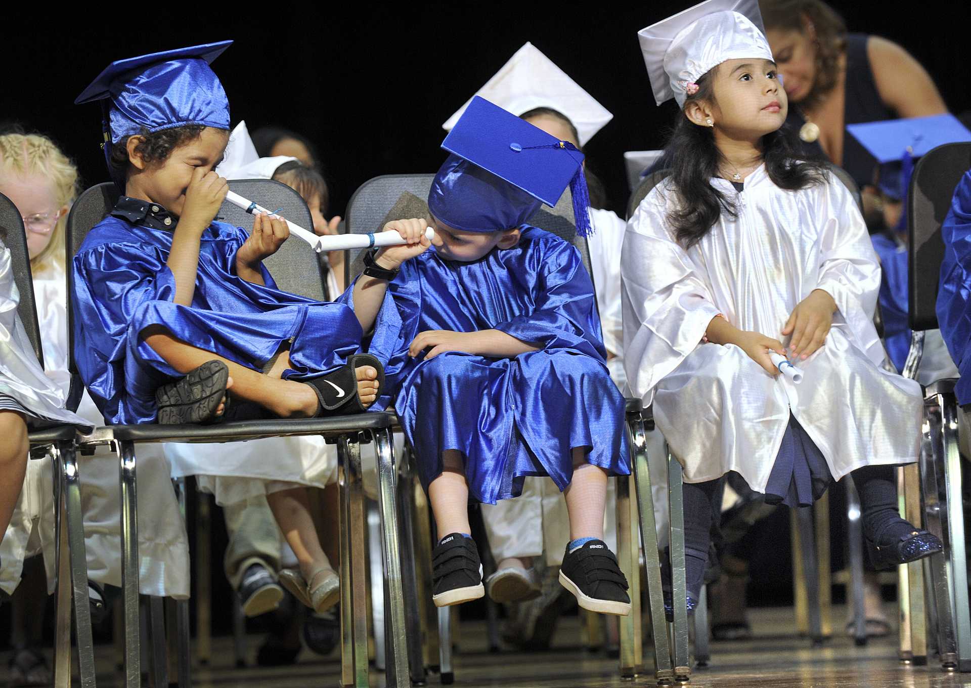 Preschoolers make telescopes out of their diplomas at their graduation ceremony.