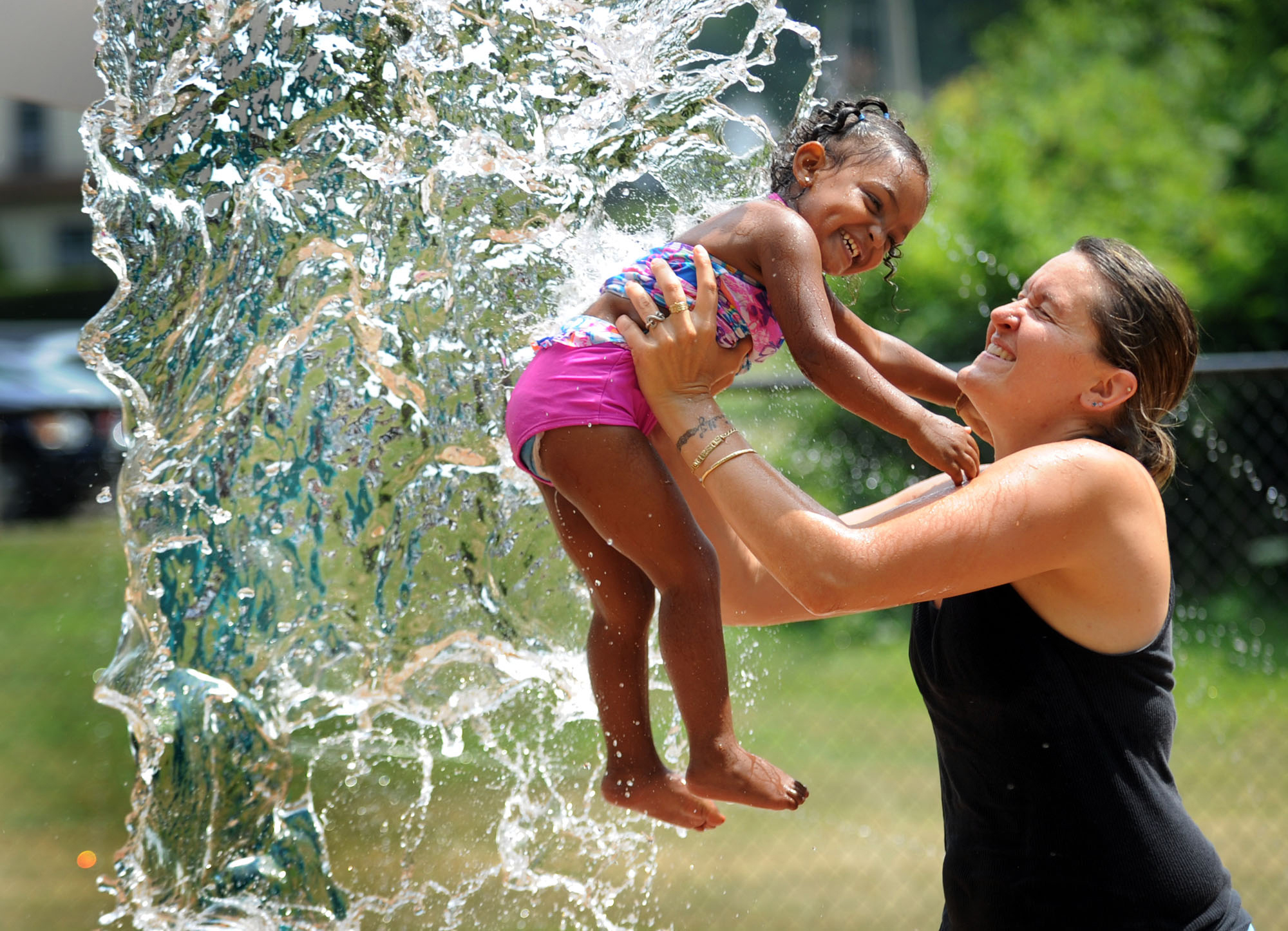 Beating a Summer heatwave, a mother lifts her daughter into the cascading water at a local splash park. 